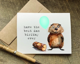 May include: A birthday card with a cartoon beaver holding a light blue balloon. The card has the text "have the best dam birfday ever" printed on it.