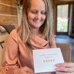May include: A white rectangular greeting card featuring five yellow stars printed in a horizontal row. Above the stars, the black text reads 5 stars. would marry again. The card is held open, displaying the printed message clearly on the front surface.