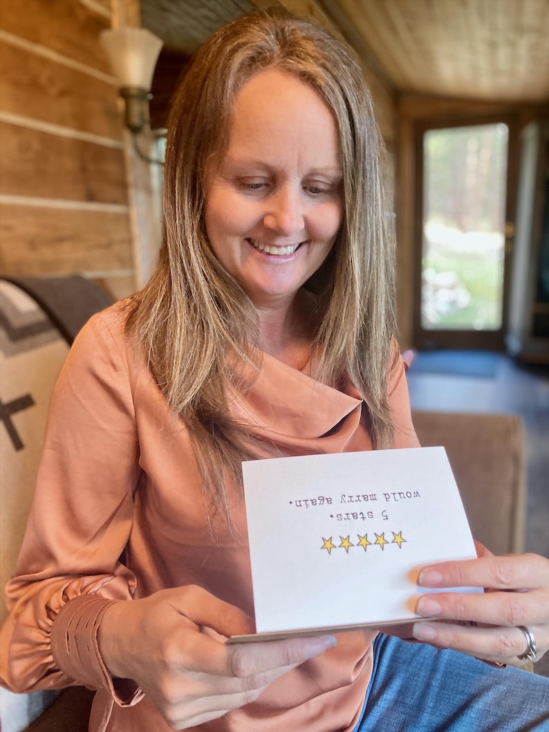 May include: A woman smiles while holding a card that says "5 stars. Would make a great gift." with five gold stars.