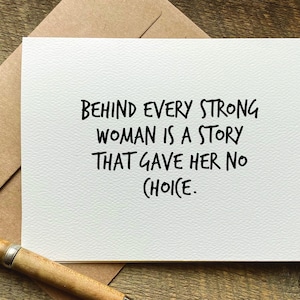 May include: White card with black text that reads "Behind every strong woman is a story that gave her no choice."