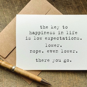 May include: A white card with black text that reads "the key to happiness in life is low expectations. lower. nope. even lower. there you go."