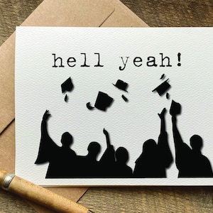 May include: A white card with black text that reads "hell yeah!" and a silhouette of a group of people throwing their graduation caps in the air.