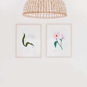 May include: Two framed botanical prints, one with a white flower and the other with a green plant. The prints are hung on a white wall.