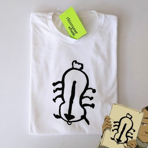 May include: White t-shirt with a black graphic of a stylized insect or creature. The shirt has a crew neck and is folded neatly. A neon green tag with the text "rhinosaur & funk" is attached to the collar.