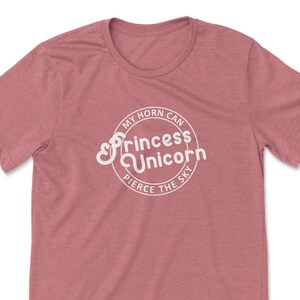 May include: A heather pink t-shirt with a white circle graphic that says "My horn can pierce the sky" and "Princess Unicorn" in a stylised font.