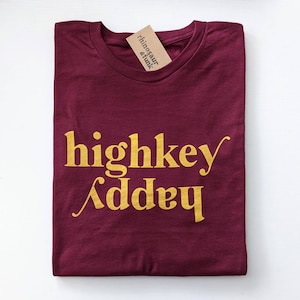 May include: Burgundy t-shirt with the text "highkey" and "addy" in gold lettering.