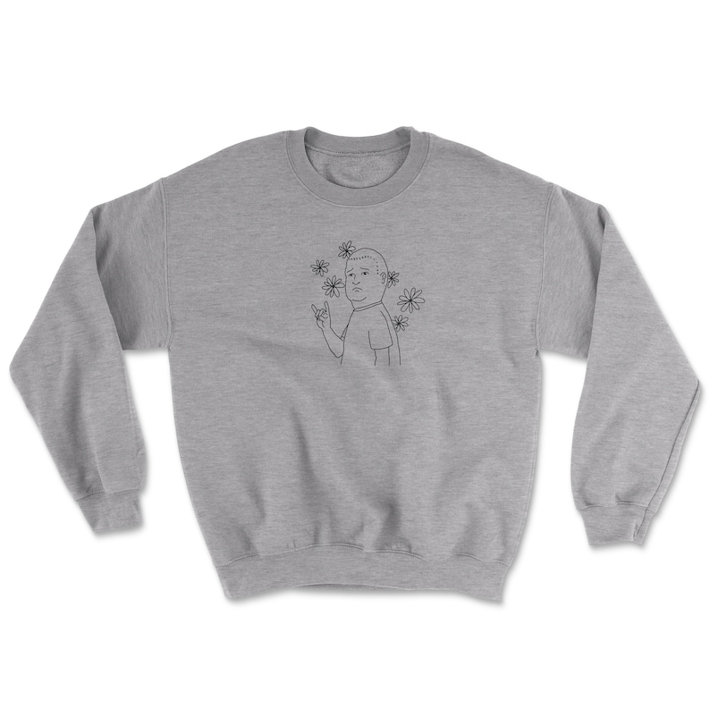 May include: A gray sweatshirt with a black line drawing of a cartoon character with a surprised expression. The character is wearing a t-shirt and has a flower crown. The character is making a rock and roll hand gesture.