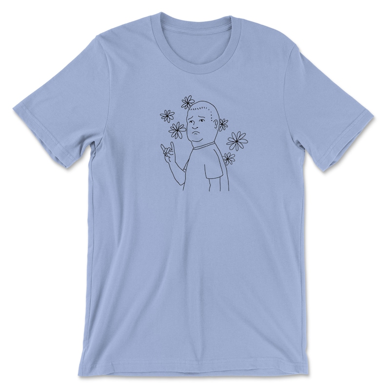 May include: A light blue t-shirt with a black line drawing of a cartoon character with a surprised expression, giving a rock and roll hand gesture. The character is surrounded by black line drawings of daisies.