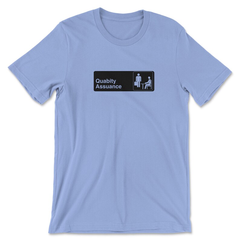 May include: Light blue t-shirt featuring a black and white graphic of a sign that reads "Quality Assurance" with a stick figure holding a briefcase and another stick figure sitting at a desk.