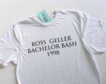 May include: White t-shirt with black text that reads "Ross Geller Bachelor Bash 1998".