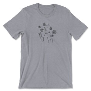 May include: A gray t-shirt with a black line drawing of a man with a surprised expression. The man is wearing a t-shirt and has flowers around his head. He is making a rock and roll hand gesture.