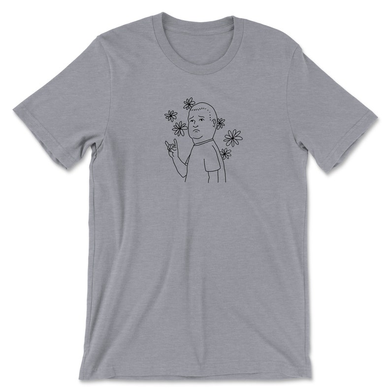 May include: A gray t-shirt with a black line drawing of a man with a surprised expression. The man is wearing a t-shirt and has flowers around his head. He is making a rock and roll hand gesture.