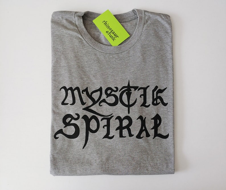 May include: Gray t-shirt with black text that reads "MYSTIC SPIRAL" in a gothic font.