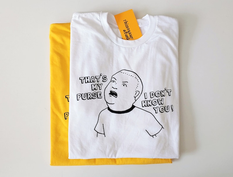May include: White t-shirt with a black and white illustration of a cartoon character with the text "That's my purse, I don't know you!"
