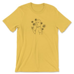 May include: A yellow t-shirt with a black line drawing of a person with a sad expression and flowers around their head. The person is making a rock and roll hand gesture.