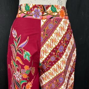 Peut inclure: Pantalon bordeaux à motifs avec une large ceinture. Le pantalon présente un motif floral sur une jambe et un motif rayé sur l'autre. La ceinture a un motif floral avec des accents orange, violets et verts.