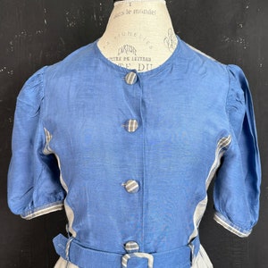 May include: A blue and white plaid dress with a blue bodice and a matching belt. The bodice has a round neckline and buttons down the front. The dress has short puffed sleeves.