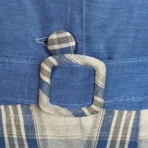 May include: A blue and white plaid fabric with a blue belt and a plaid button. The fabric has a woven texture.