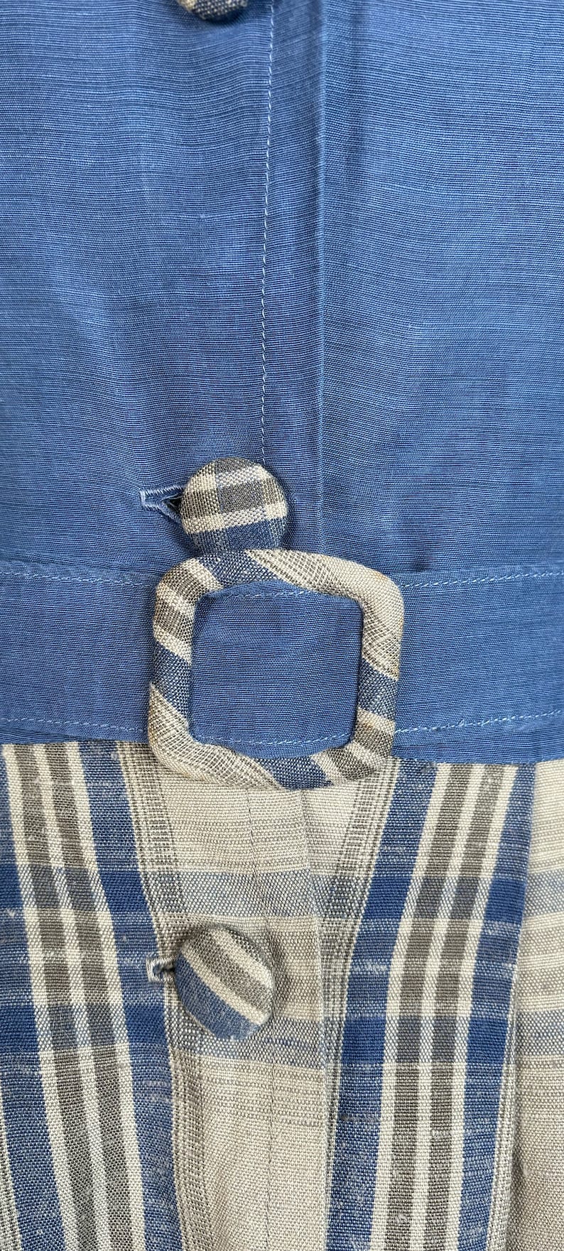May include: A blue and white plaid fabric with a blue belt and a plaid button. The fabric has a woven texture.