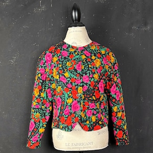 Könnte beinhalten: Knopfjacke mit floralem Muster. Die Jacke hat einen schwarzen Hintergrund, bedeckt mit rosa, roten und gelben Rosen mit grünen Blättern. Sie wird auf einer Schaufensterpuppe präsentiert. Vintage-Stil.