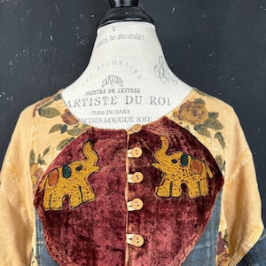 Puede incluir: Una blusa de terciopelo marrón con cierre de botones y dos elefantes bordados. La blusa está decorada con un estampado floral y tiene un diseño de patchwork.