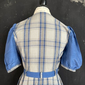 May include: A plaid dress with a blue belt and blue puffed sleeves. The dress is made of a light-weight fabric and has a vintage style.