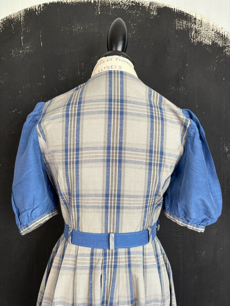 May include: A plaid dress with a blue belt and blue puffed sleeves. The dress is made of a light-weight fabric and has a vintage style.