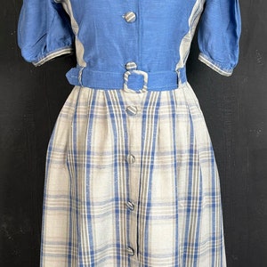 May include: A blue and white plaid dress with a blue bodice and a white and blue plaid skirt. The dress has a button-up front and a belt.