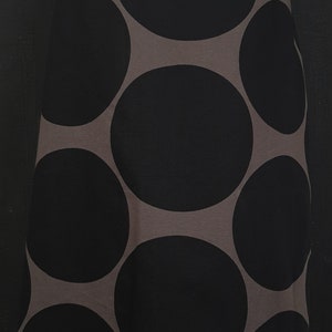 May include: A knee-length skirt featuring a large-scale polka dot pattern in black against a dark taupe background. The skirt has a fitted waistband and a straight silhouette, with a visible fringe detail along the bottom hemline of the garment.