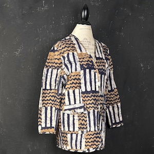 May include: A long-sleeved jacket featuring a repeating pattern of vertical stripes and horizontal zigzag lines in shades of navy blue, tan, and white. The jacket has a V-neckline, a button-front closure, and a single visible front pocket.