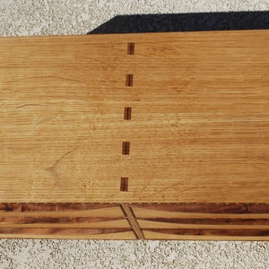 May include: A handcrafted wooden chest with a light brown finish. The chest features dovetail joints and a series of curved drawers. The wood grain is visible, adding to the natural aesthetic. The chest is rectangular in shape.