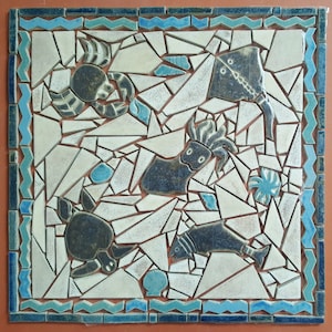 Può includere: Una piastrella di ceramica bianca con un bordo blu presenta un motivo a mosaico di varie creature marine, tra cui un granchio, una raia, un polpo, una tartaruga e un pesce. La piastrella è realizzata con piccoli pezzi irregolari di ceramica in tonalità di bianco, blu e nero.