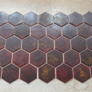 May include: A row of hexagonal tiles in shades of brown, red, and gold. The tiles have a slightly textured surface and a glossy finish.