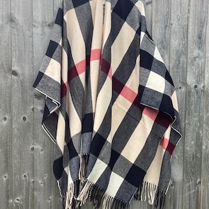 May include: A black, white, and red plaid poncho with fringe trim. The poncho is made of a soft, warm fabric and is perfect for layering in the fall or winter.