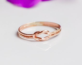 May include: A rose gold ring featuring a knot design. The ring is simple and elegant.
