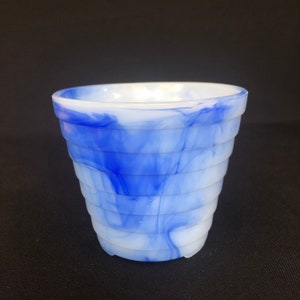 Op de afbeelding: Een witte en blauwe swirl glazen plantenpot met een geribbeld ontwerp. De pot is gemaakt van ondoorzichtig glas met een blauw en wit marmerpatroon.