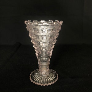 Könnte beinhalten: Eine klare Glasvase mit rosa Tönung und geometrischem Muster. Die Vase hat einen breiten Boden und einen schmalen Hals.