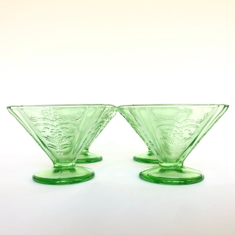 May include: Set of four green glass dessert dishes with a floral design. The dishes have a flared rim and a pedestal base.