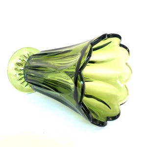 Puede incluir: Un jarr&oacute;n de vidrio verde con un borde acampanado en forma de p&eacute;talo. El jarr&oacute;n tiene una base redonda y un dise&ntilde;o texturizado y acanalado. El vidrio es de color verde transl&uacute;cido y el jarr&oacute;n est&aacute; sobre un fondo blanco.