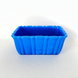Puede incluir: Un pequeño macetero rectangular azul con un diseño acanalado. El macetero está hecho de plástico y tiene un acabado liso y brillante.