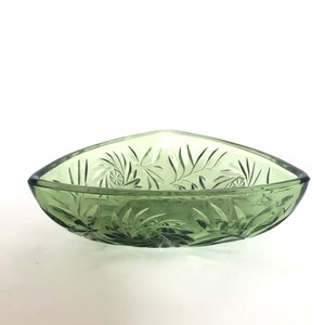 May include: A triangular green glass bowl with a decorative etched pattern. The bowl is made of clear glass with a green tint.