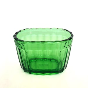 Può includere: Una ciotola quadrata di vetro verde con bordo smerlato. La ciotola presenta dettagli a coste verticali sui lati e una base quadrata. Il vetro è trasparente. Ideale per servire.