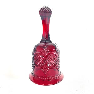 May include: A decorative ruby red glass bell with a textured surface and a long handle. The bell features a detailed pattern of diamonds and floral designs. The bell is a decorative item.