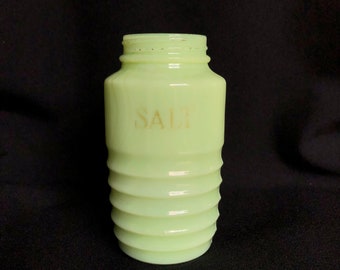 May include: A pale green glass salt shaker with a ribbed design and the word "SALT" printed in gold on the front.
