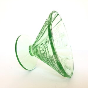 May include: A green glass footed bowl with a delicate floral design. The bowl is made of Depression glass and has a vintage look.