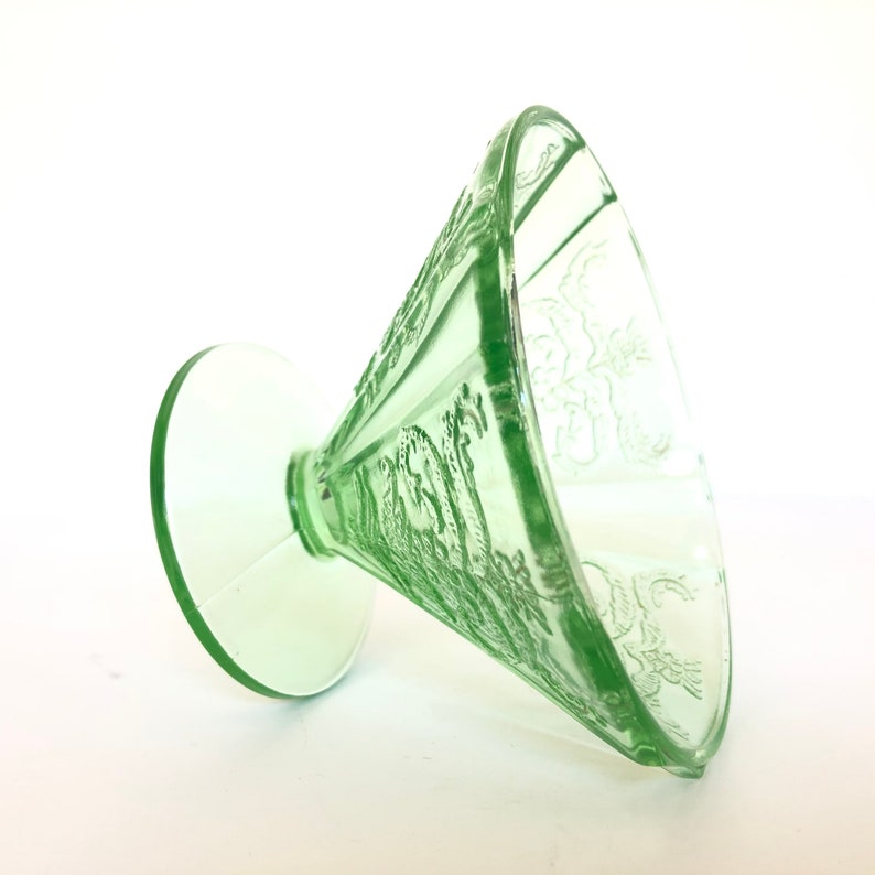 May include: A green glass footed bowl with a delicate floral design. The bowl is made of Depression glass and has a vintage look.