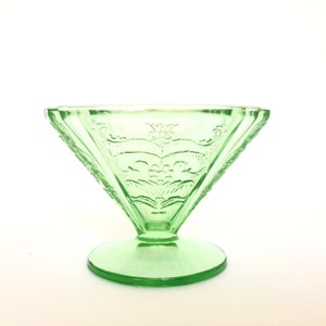 May include: A green glass bowl with a footed base and an intricate floral design. The bowl is made of Depression glass and has a vintage look.