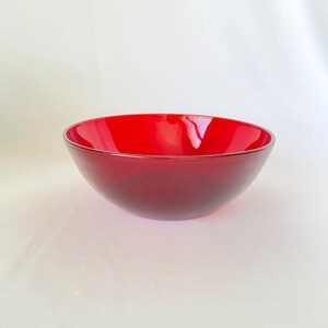 Puede incluir: Un cuenco rojo brillante con un borde plateado. El cuenco tiene un diseño liso y curvado y un color rojo intenso que se desvanece ligeramente hacia la base. El cuenco es probablemente de vidrio o un material similar.