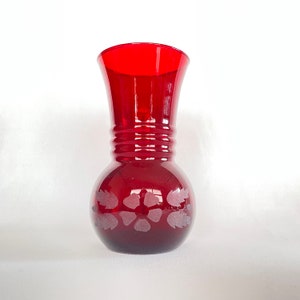 May include: A red glass vase with a frosted floral design. The vase has a wide mouth and a rounded base.