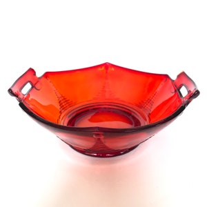 Peut inclure: Un bol de service en verre rouge avec deux poignées. Le bol a un design texturé et une forme carrée.